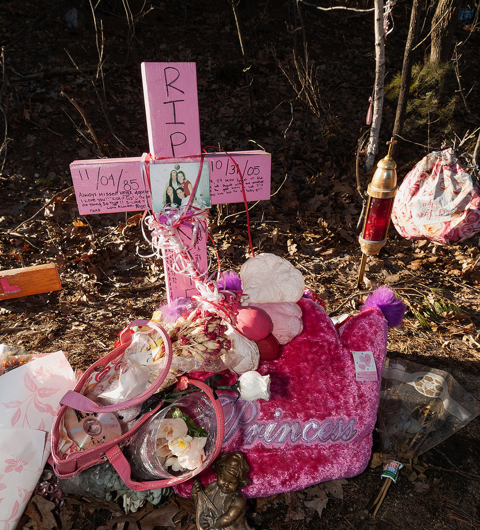 A pink wooden roadside memorial cross decorated with flowers, photographs, and ribbons at an accident scene in Salem, New Hampshire