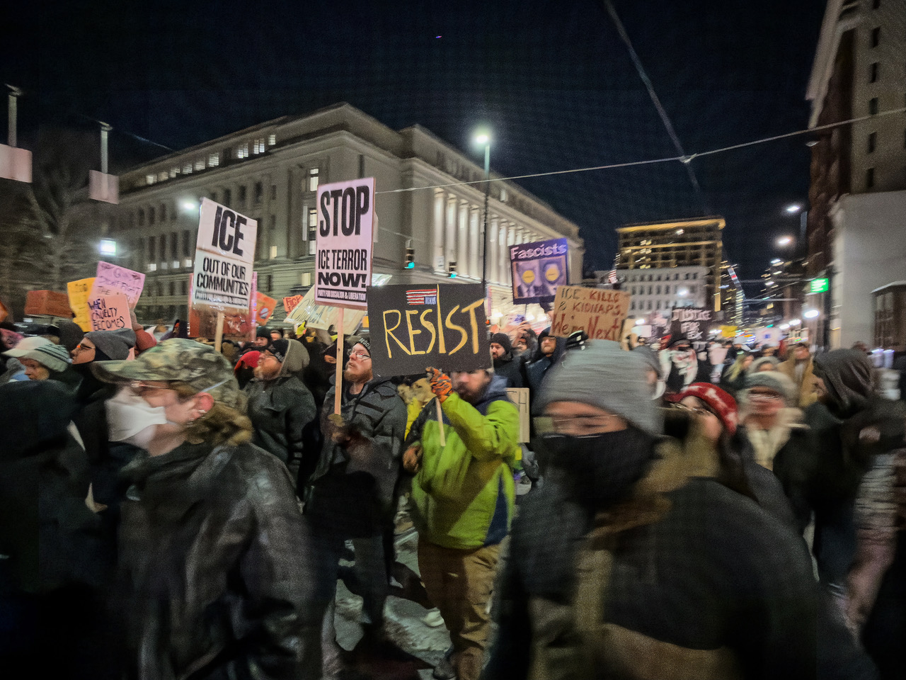 Nighttime protest march with hand-painted signs reading Resist and Stop Ice Terror Now in downtown Cincinnati