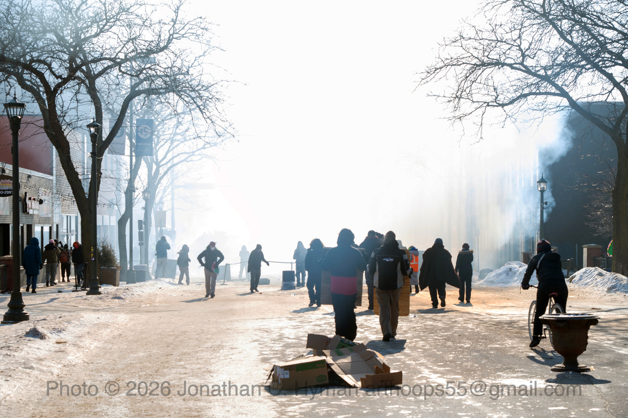 Protesters walking through a smoky, sunlit winter street in Minneapolis after tear gas was deployed