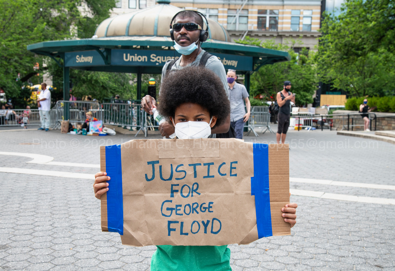A young masked demonstrator holding a cardboard Justice for George Floyd sign at Union Square