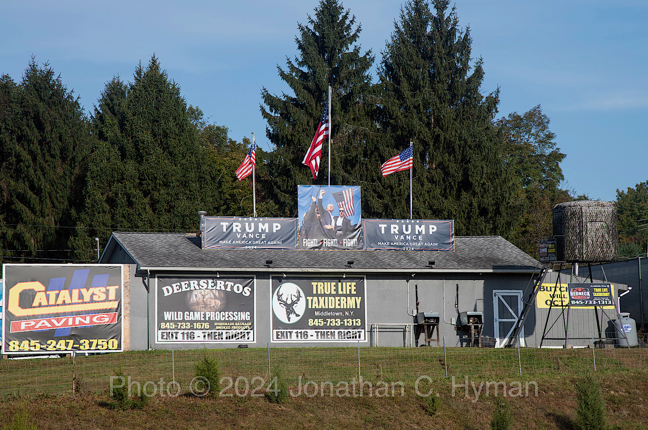 Trump Vance banners and a Fight Fight Fight photograph mounted on the roof of a taxidermy and game processing shop with American flags