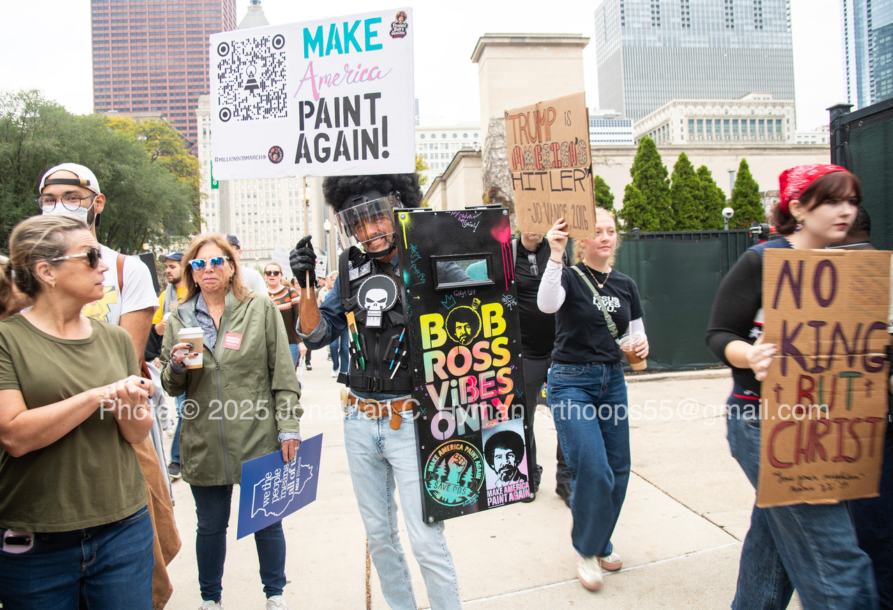 Demonstrator carrying a hand-painted 'Bob Ross Vibes Only' shield among protest signs at a Chicago rally