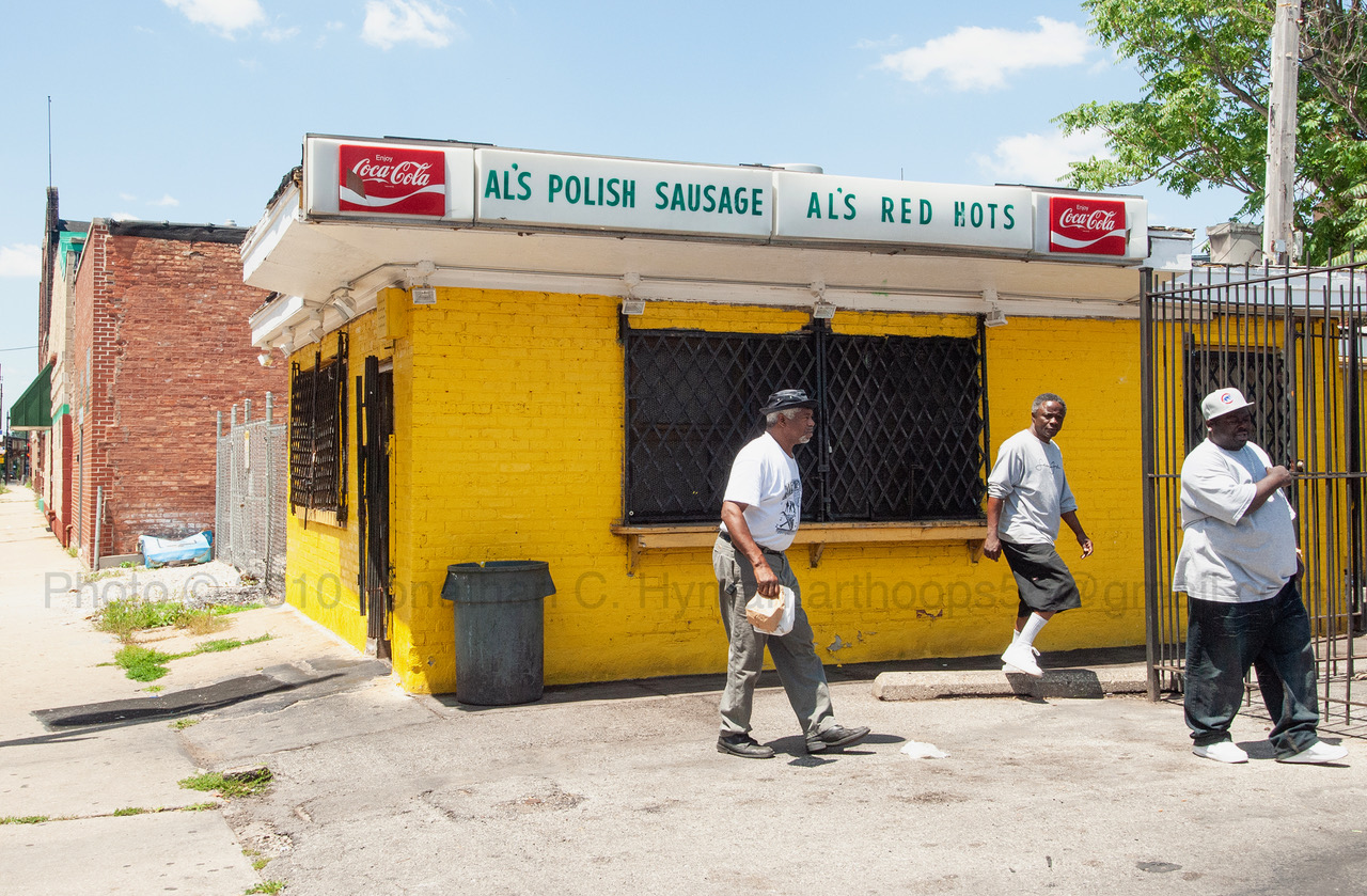 Pedestrians walking past Al's Polish Sausage and Al's Red Hots, a yellow brick hot dog stand in Chicago